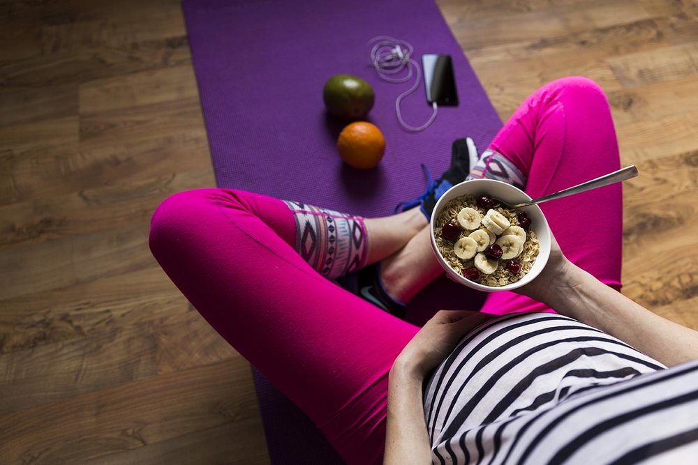 pregnant woman eating healthy while sitting on yoga mat